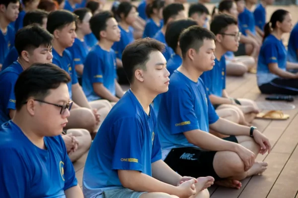 People in matching blue shirts sit cross-legged on a wooden floor, meditating.
