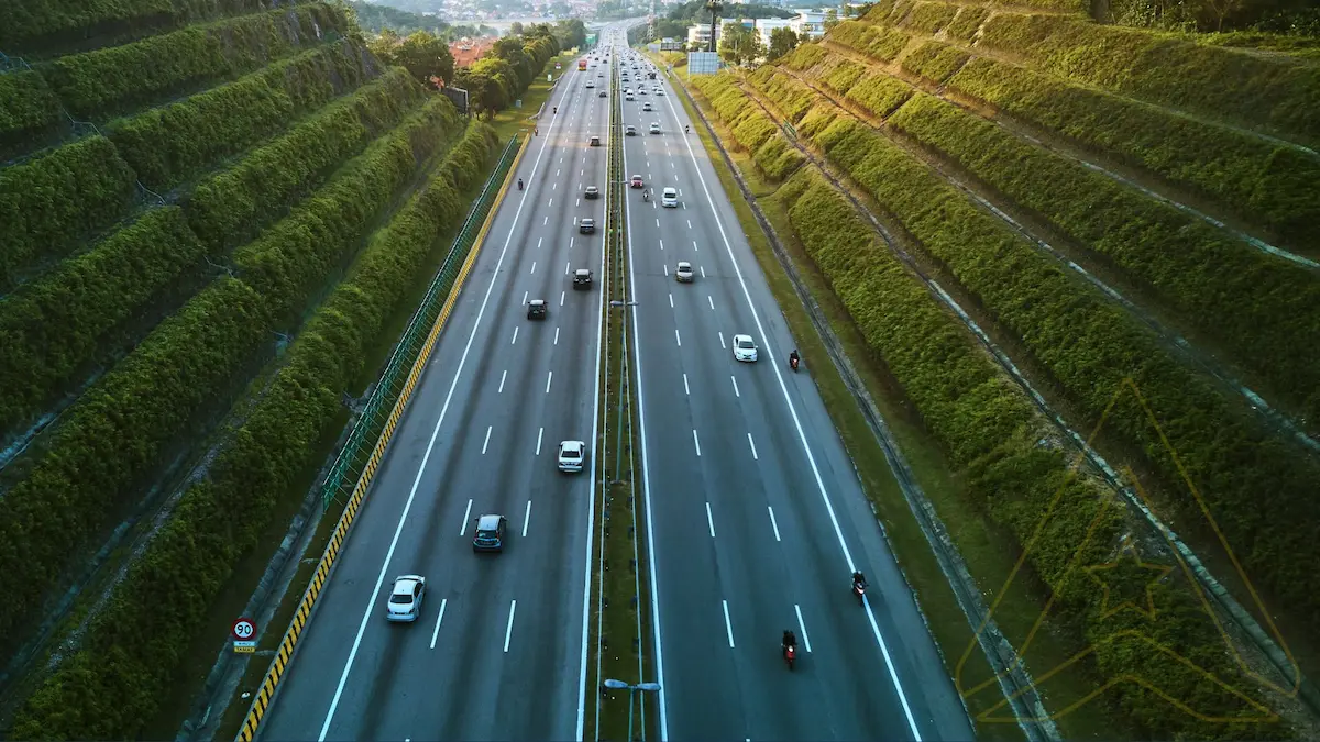 Aerial view of a highway with cars and motorcycles, bordered by terraced green hills.