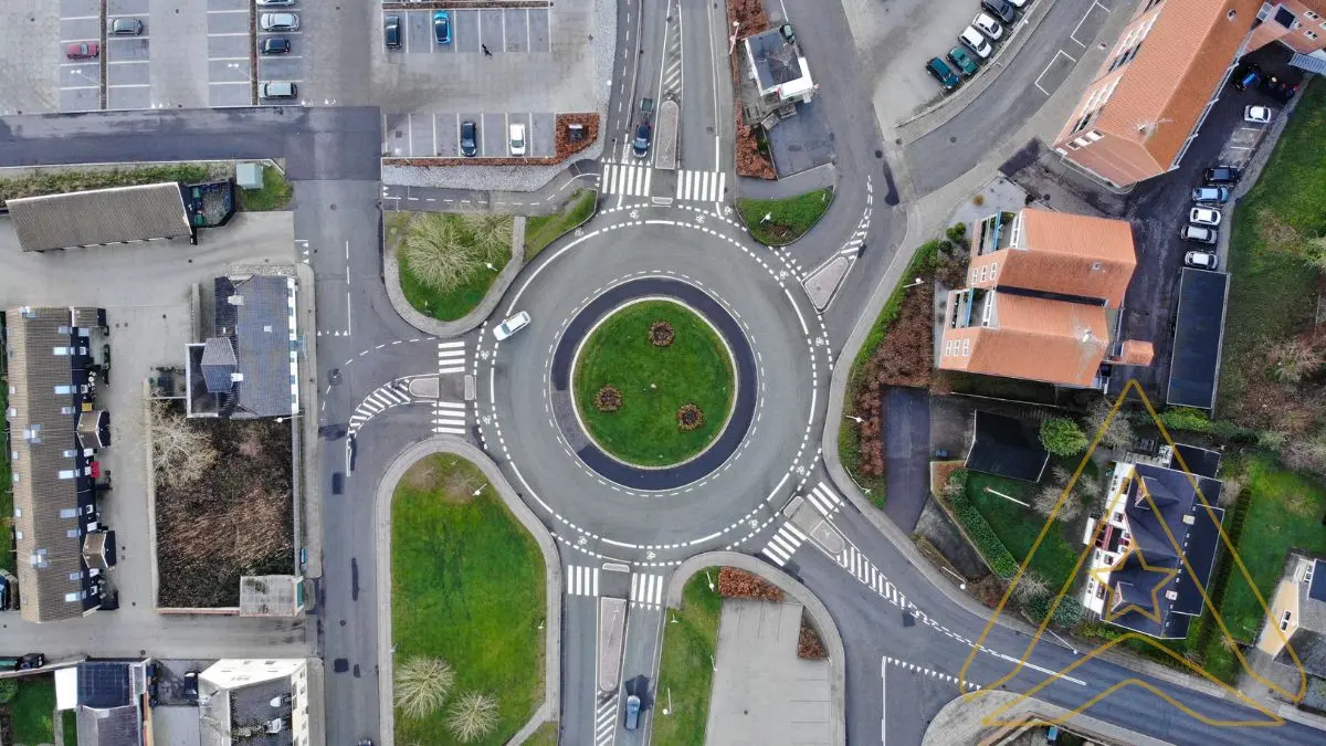 Aerial view of a roundabout with four connecting roads, surrounded by buildings and green areas.