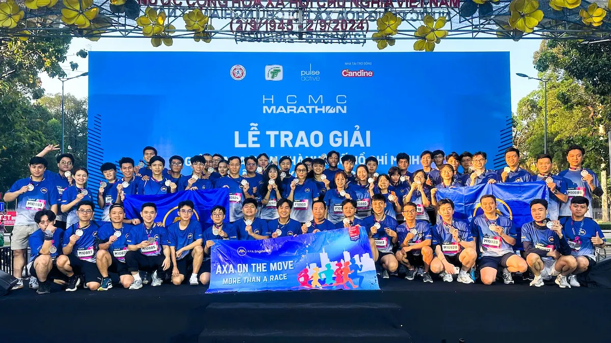 Group of runners in blue shirts onstage with banners, medals, AXANH tuyển dụng logo.
