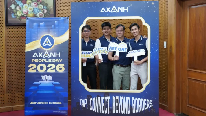 Four men stand in a blue photo frame prop at AXANH People Day 2026, holding signs.