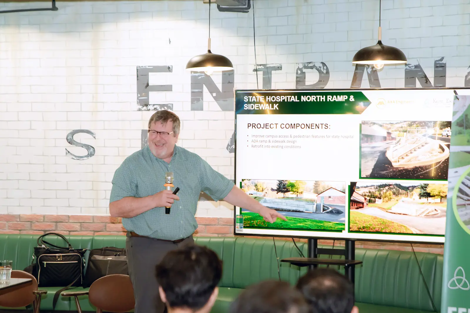Man in green shirt presents hospital ramp project on screen to audience.