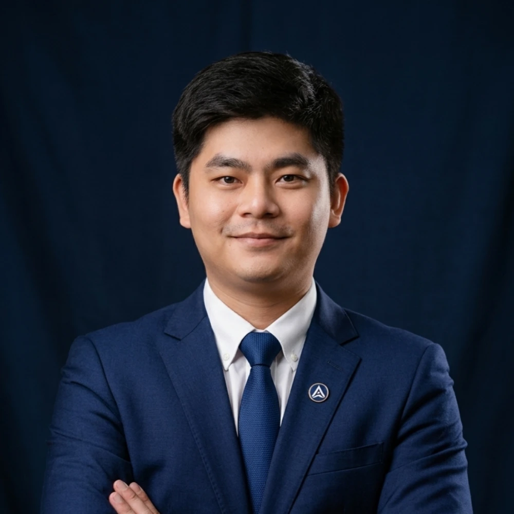 Man in blue suit and tie, arms crossed, smiling before dark blue background.