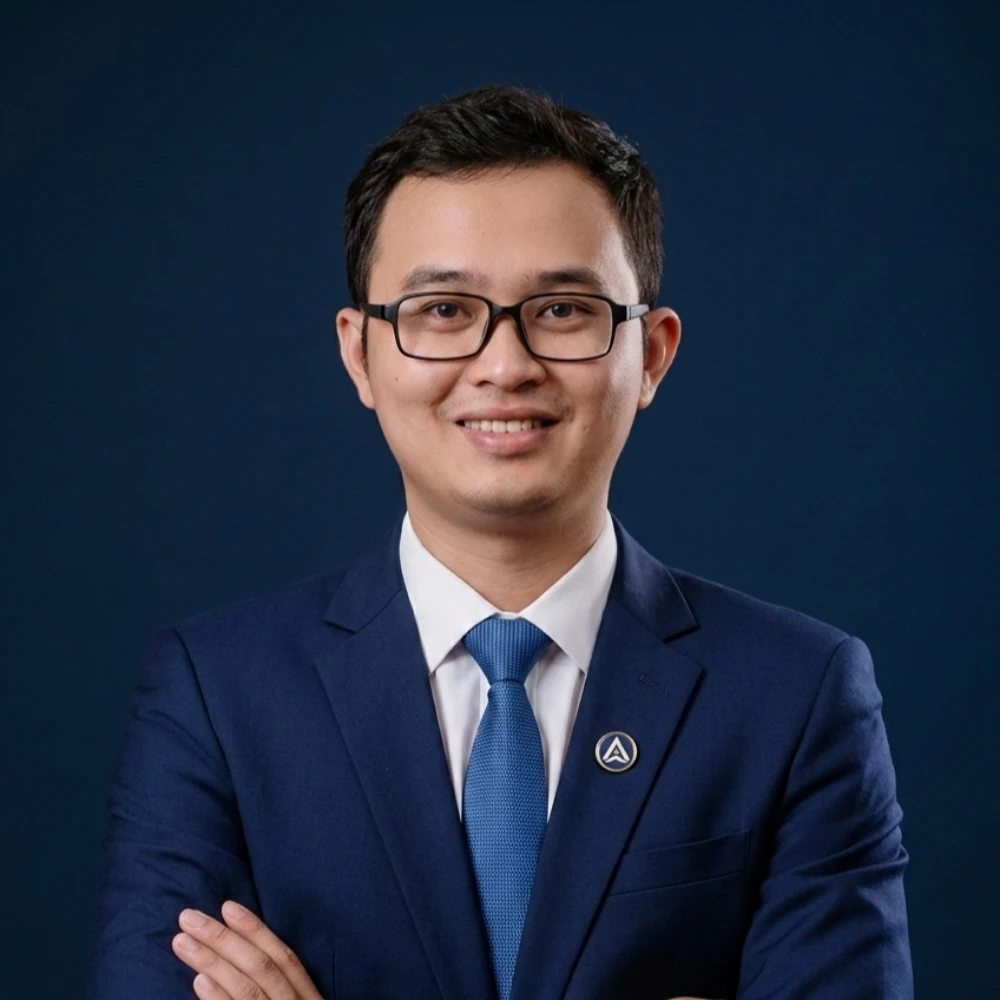 Man in blue suit and glasses, arms crossed, smiling against dark blue background.