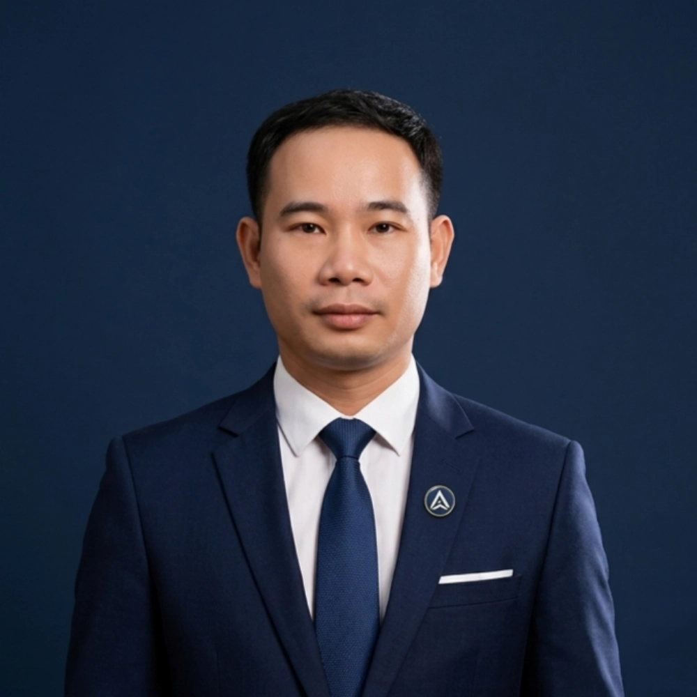Man in navy suit with pin poses against dark blue background, looking serious.