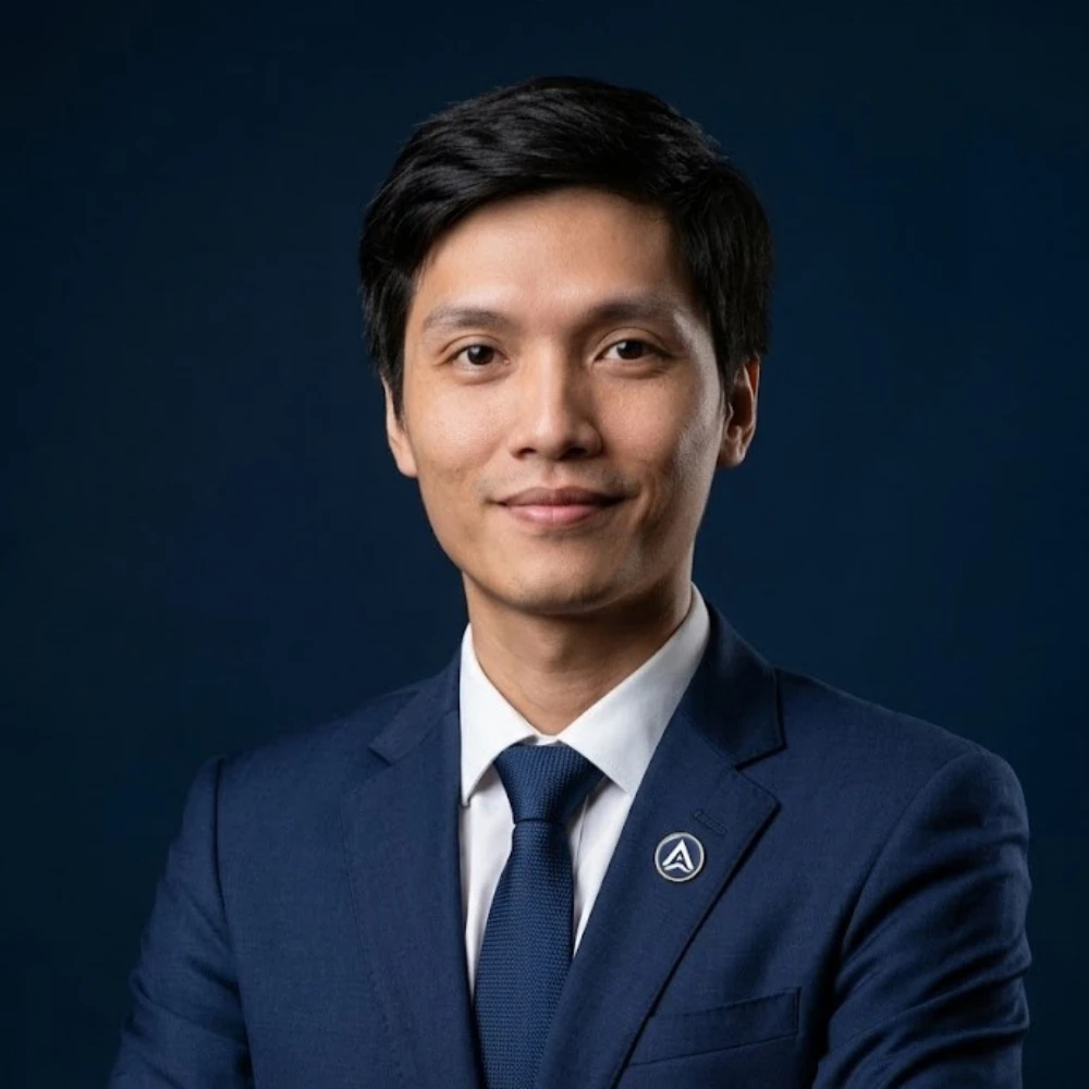 Man in dark blue suit and tie, arms crossed, smiling softly.
