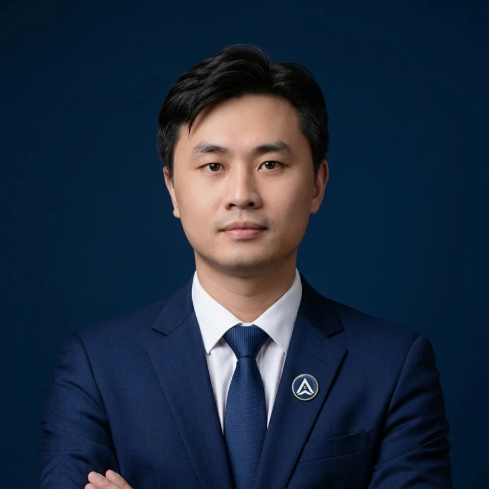 Man in navy suit with arms crossed, wearing AXANH logo pin, neutral expression.