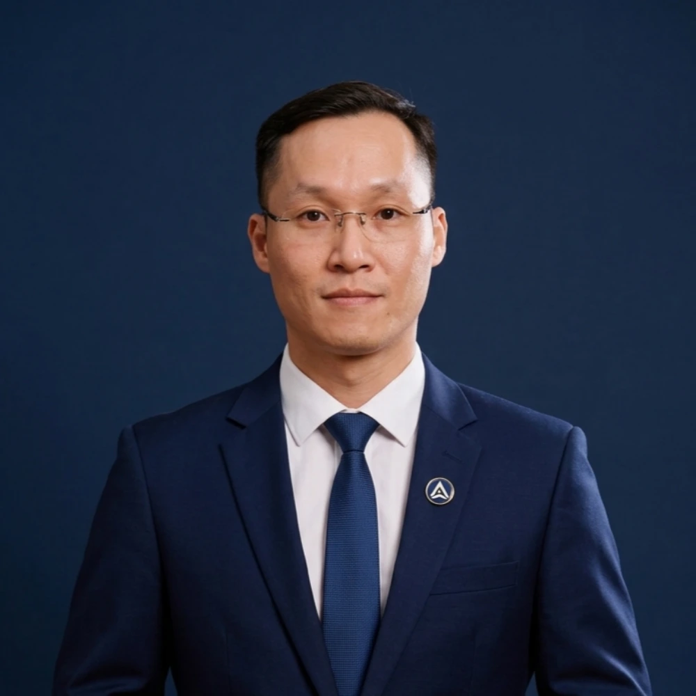 AXANH leadership team member in blue suit and glasses, plain dark background.