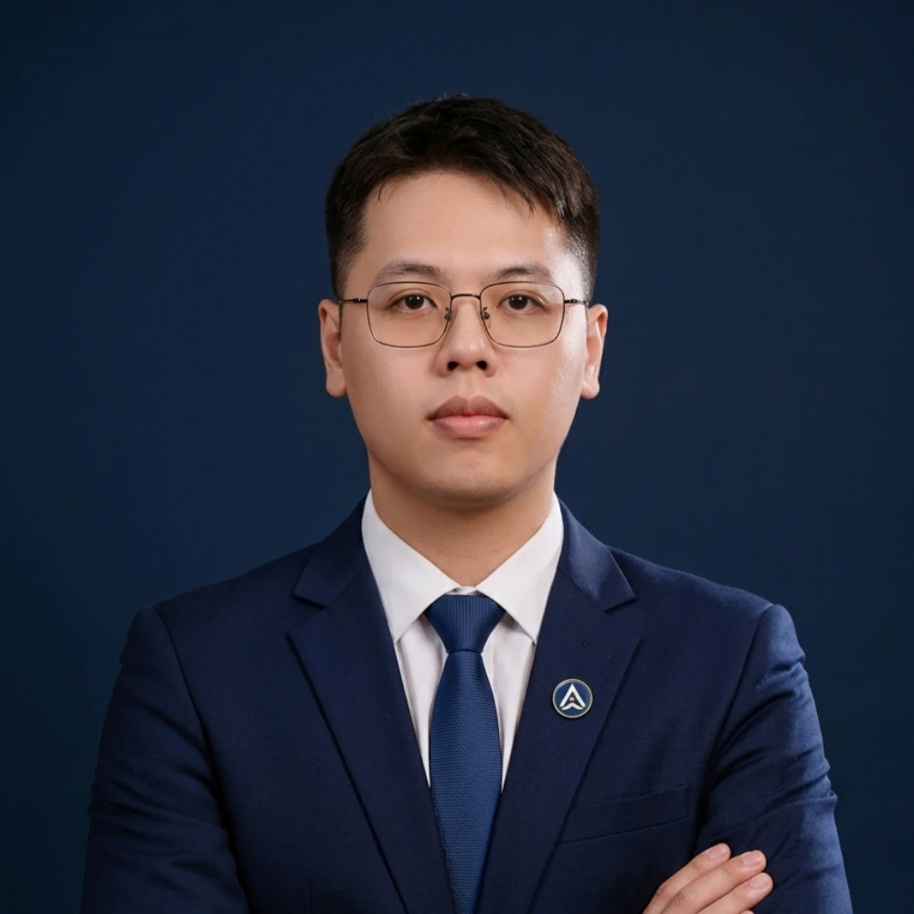 AXANH leader in navy suit, arms crossed, glasses, short hair, dark background.