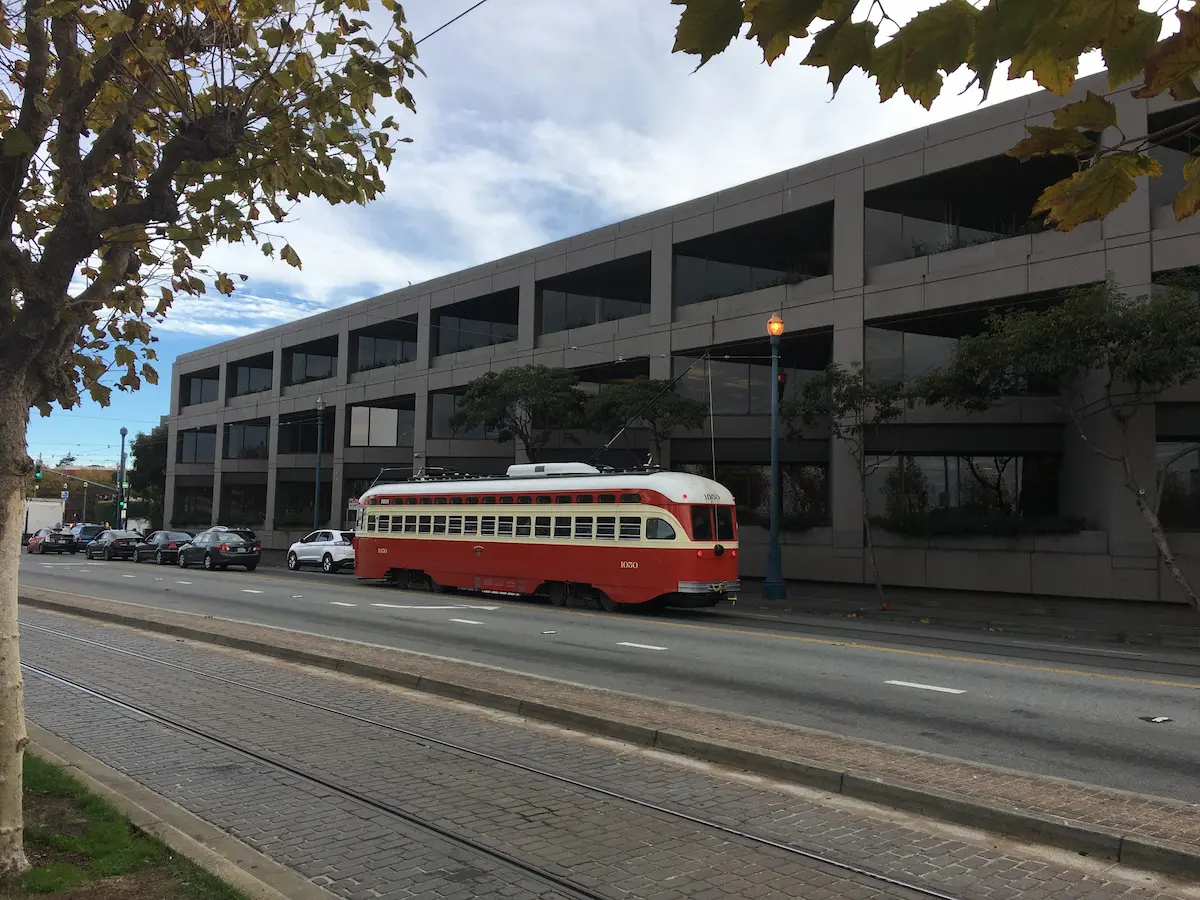 Red and white vintage streetcar on city street with autumn trees and cars.