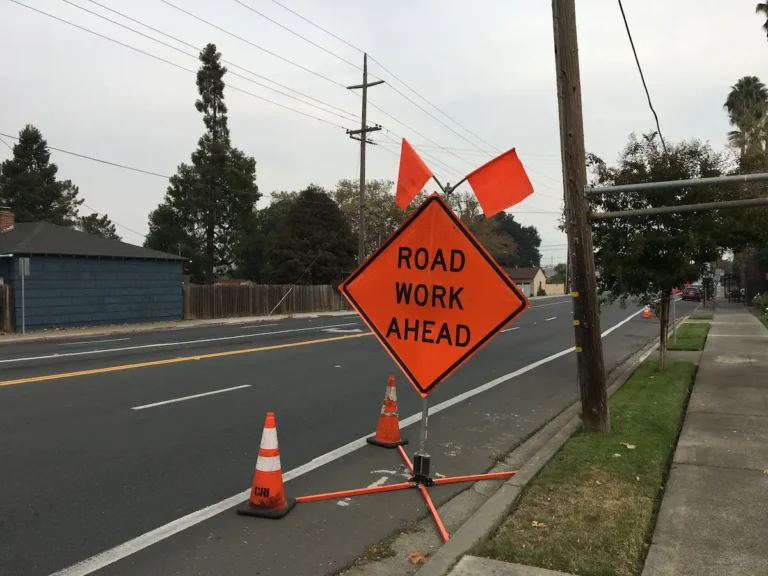 Orange Road Work Ahead sign with flags and cones on a quiet street.