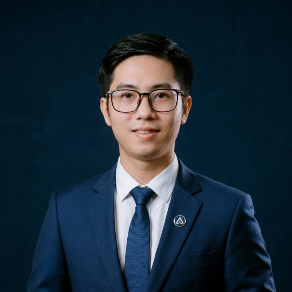 Man in glasses, navy suit, white shirt, and blue tie on dark background.
