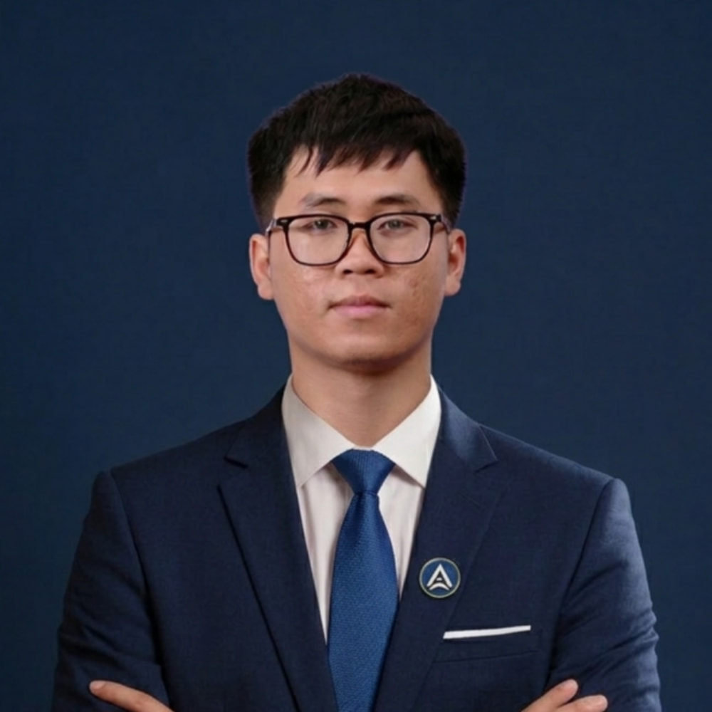 Man in navy suit and glasses stands with arms crossed on dark blue background.