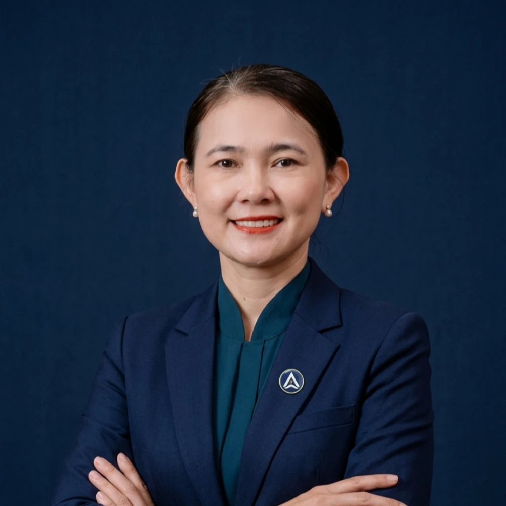Woman in navy blazer and teal blouse, arms crossed, smiling against dark background.