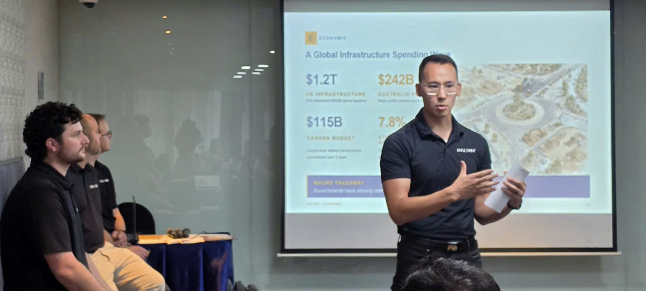 A man presents in front of a slide on global infrastructure spending; two listen.
