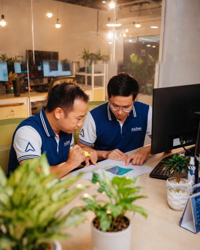 Two men in blue uniforms review documents at a desk in an office.