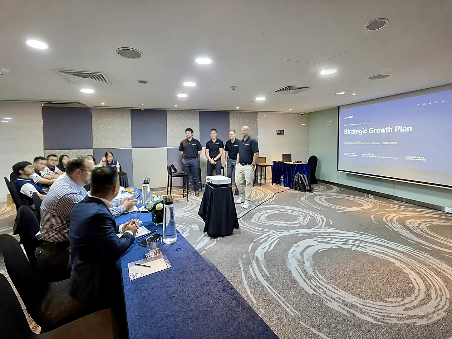 People in business attire watch a Strategic Growth Plan presentation with four speakers.