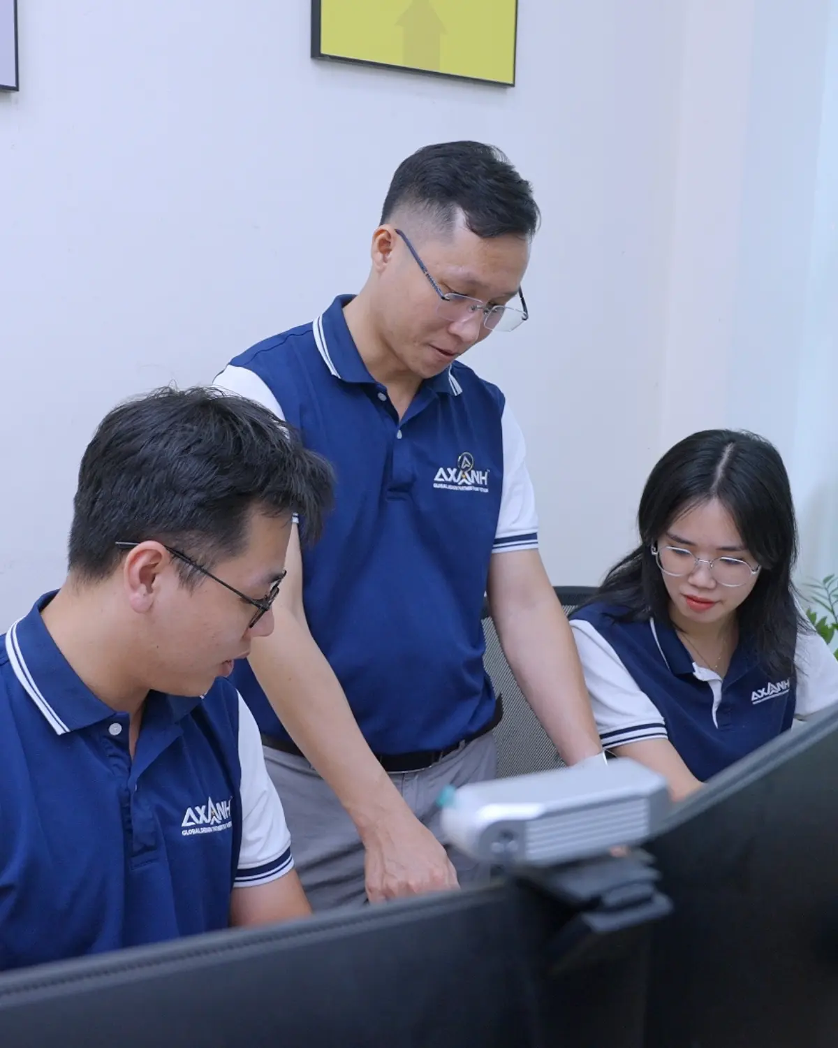 Three people in blue shirts work together at a desk with documents.